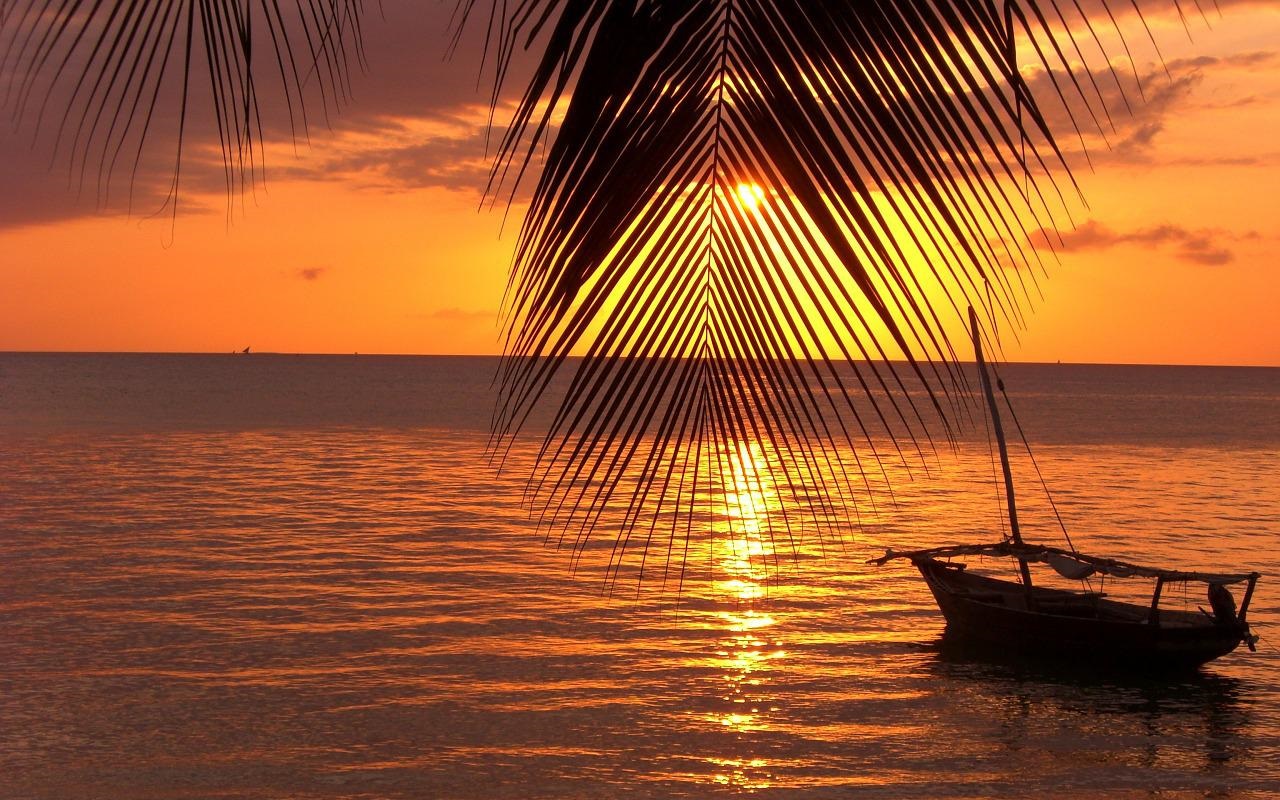 Vendite aperte Natale e Capodanno 2022/2023. barca sul mare al tramonto con foglia di palma.
