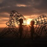 Partecipa al Burning Man festival. Sculture di due bambini dentro a due gabbie da adulti nel deserto.