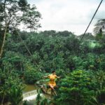 Viaggio a Bali 2023. Donna vestita di giallo in altalena sopra le foreste verdeggianti di Bali.