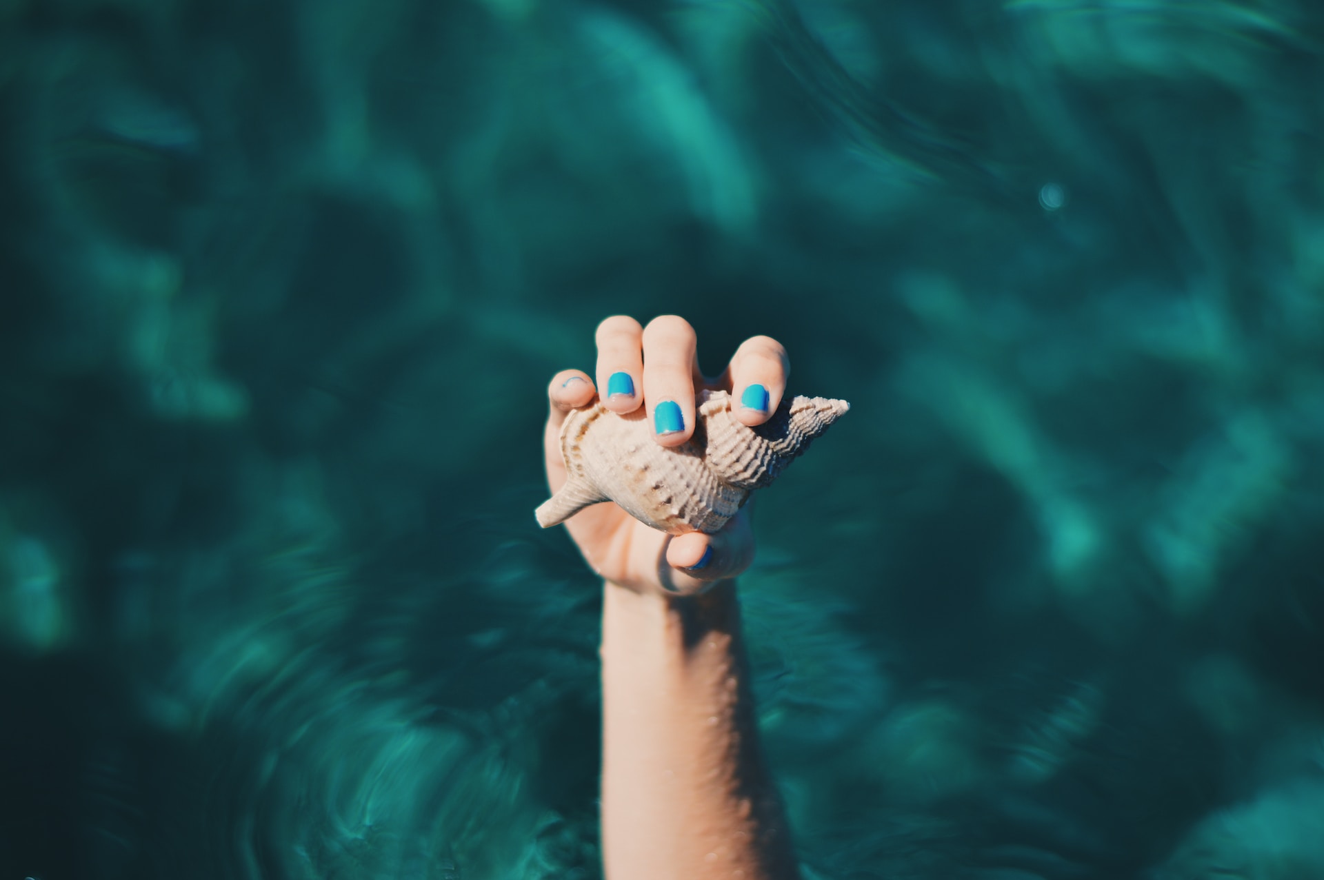 Dove andare alle Baleari 2023. Mare sullo sfondo, in primo piano mano con conchiglia e smalto azzurro.