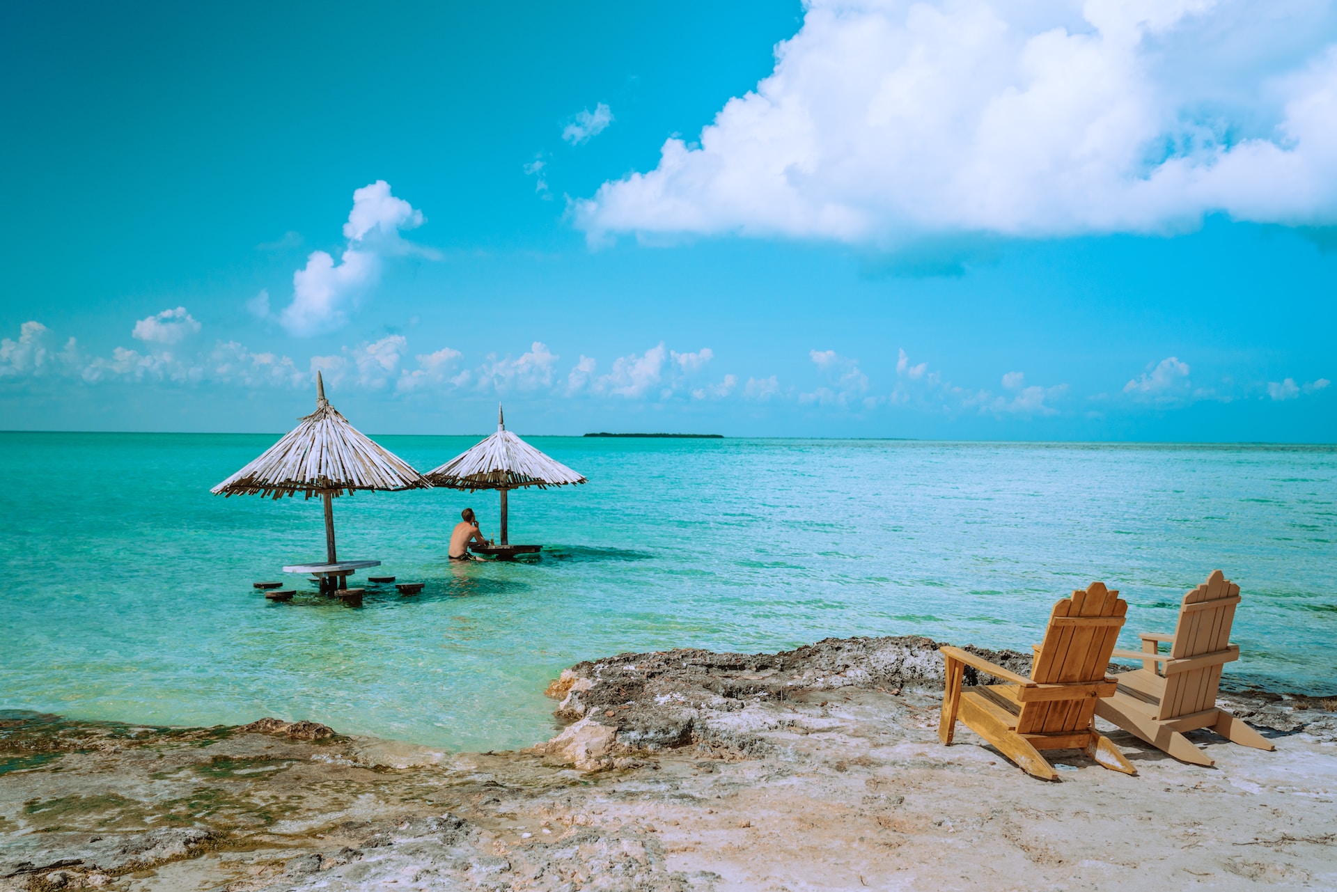 Esplora la barriera corallina del Belize. vista del mare, due lettini in legno a riva, due ombrelloni e una persona in acqua.