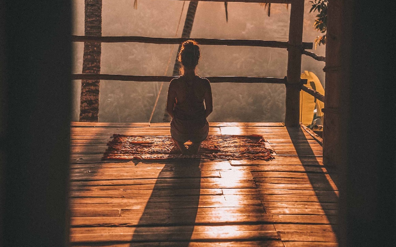 Ritiro Yoga a Venezia. Ragazza che medita al tramonto su pavimento di legno, davanti a un paesaggio.