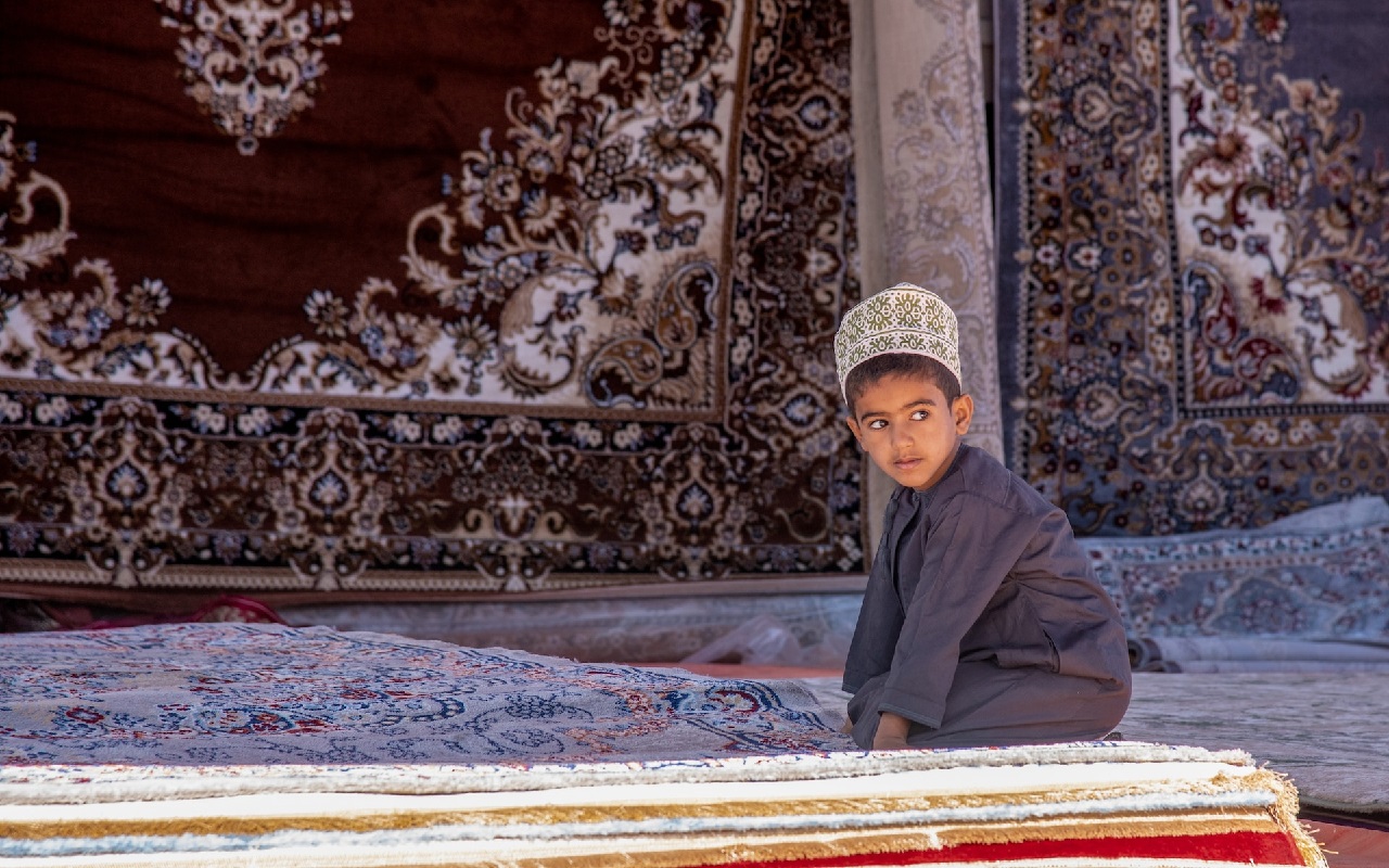Oman di lusso 2024. Bambino omanita con vestiti tradizionali, inginocchiato sopra un tappeto.