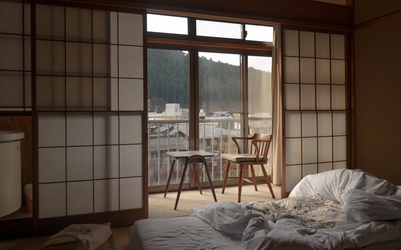 Dormire in un Ryokan in Giappone. Un futon in una stanza con due sgabelli, una parete in carta di riso e vista sulla città.