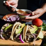 Migliori tacos a Città del Messico. Tacos su un tagliere, con mani che riempiono tacos sullo sfondo.