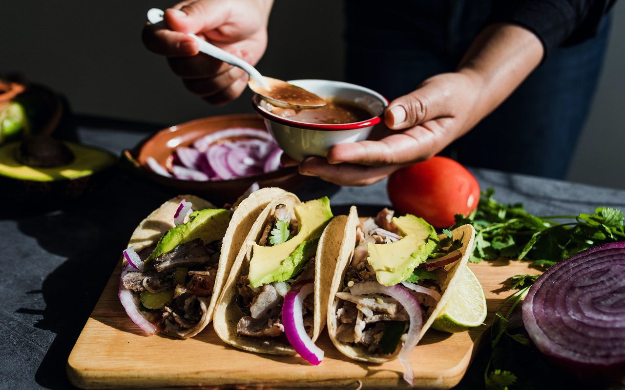 Migliori tacos a Città del Messico. Tacos su un tagliere, con mani che riempiono tacos sullo sfondo.