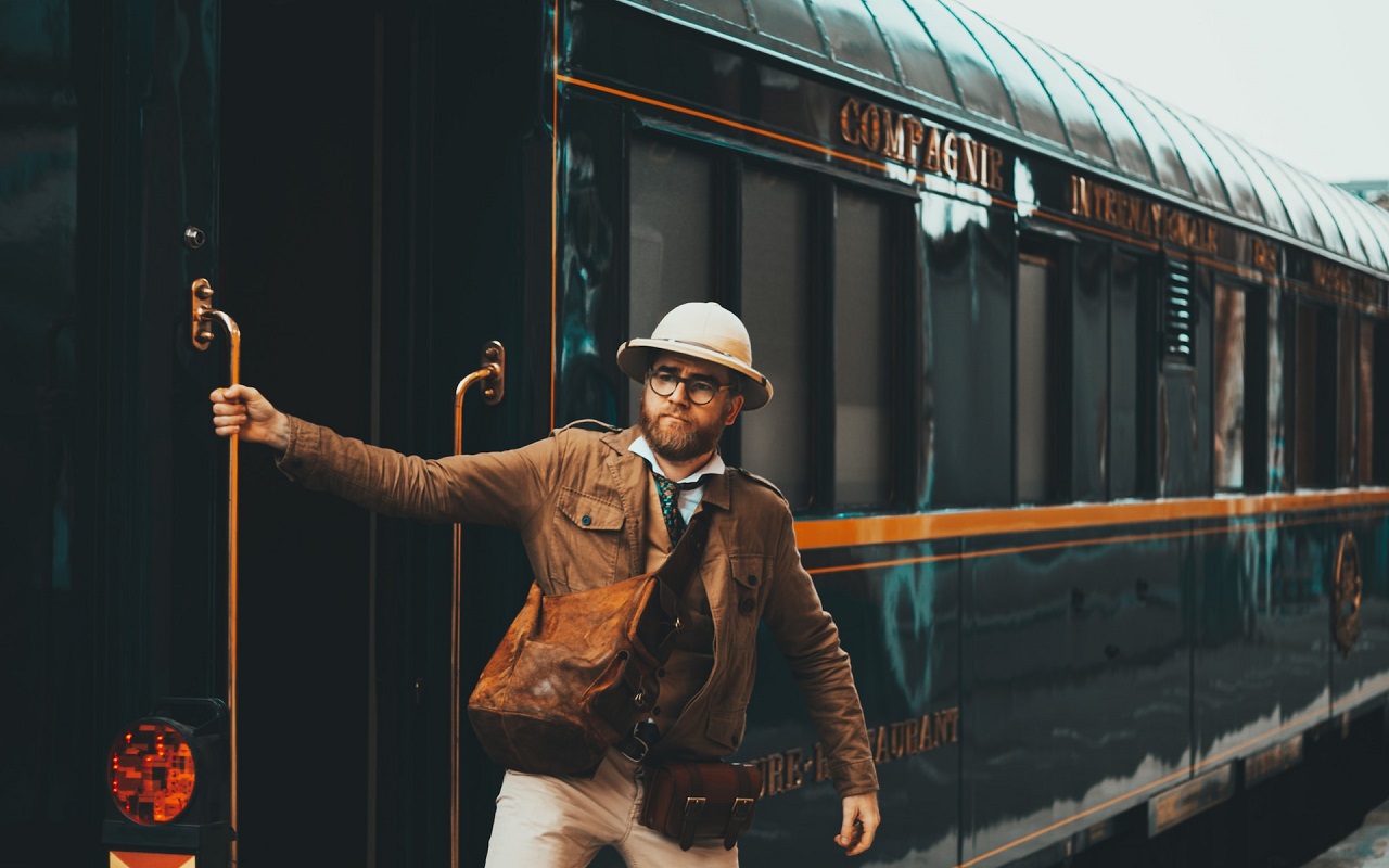 Viaggio sull'Orient Express 2024. Ragazzo in abbigliamento da safari urbano scende da un treno antico.